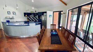 A modern kitchen with a central island, wooden dining table, and large windows. - La Block Yallingup simply the best! (Yallingup)