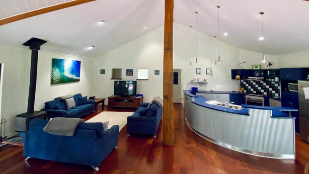 A spacious living area with a high ceiling, wooden beams, a kitchen with blue cabinets, and a large TV. - La Block Yallingup simply the best! (Yallingup)