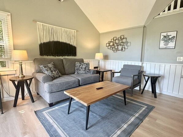 Ein Wohnzimmer mit einer Couch, einem Couchtisch, zwei Beistelltischen, einer Lampe und einem Wandbild.