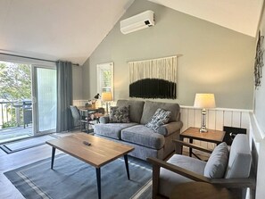 Ein modernes Wohnzimmer mit einer Couch, einem Couchtisch und Lampen. Ein Schiebeglasfenster führt in einen Außenbereich.