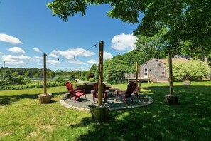 A circular outdoor seating area with chairs and a table, surrounded by grass and trees, with a house in the background.