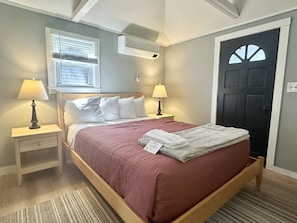 A bedroom with a bed, two bedside tables with lamps, a window, and a door.