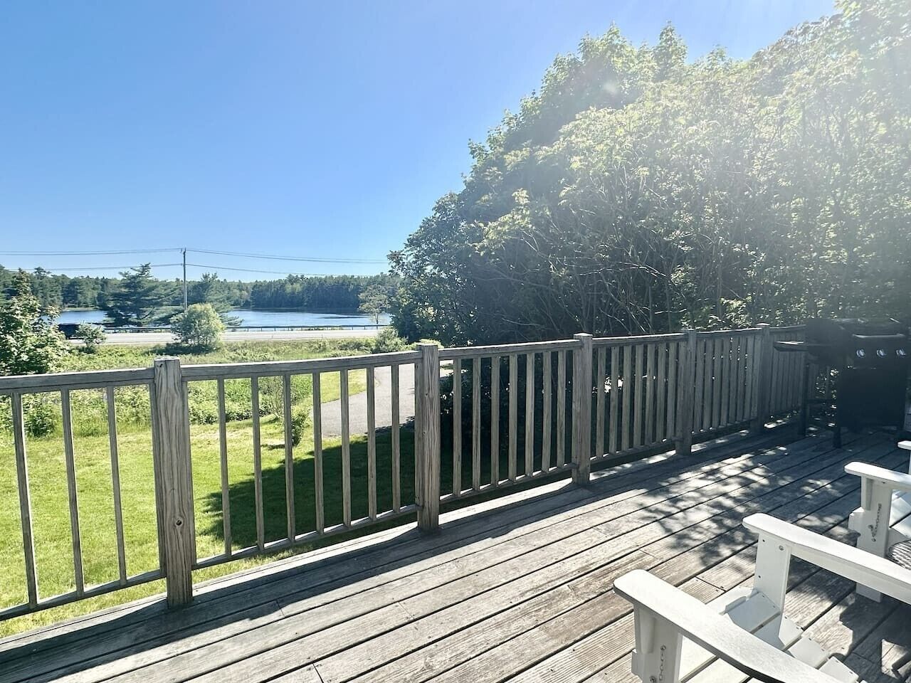A wooden deck with a railing, overlooking a grassy area and a body of water.