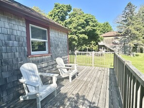 A wooden deck with two Adirondack chairs, a window, and a fenced yard.