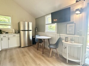 Eine moderne Küche mit einem Edelstahl-Kühlschrank, einem runden Esstisch mit zwei Stühlen und einem kleinen, weißen Beistelltisch mit einer Pflanze.