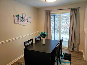 Enjoy meals in this cozy dining area with a wooden table and comfortable chairs, surrounded by beautiful artwork and a lovely view.