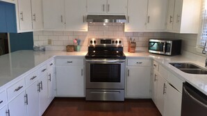 A modern kitchen with white cabinets, stainless steel appliances, and a wooden floor.
