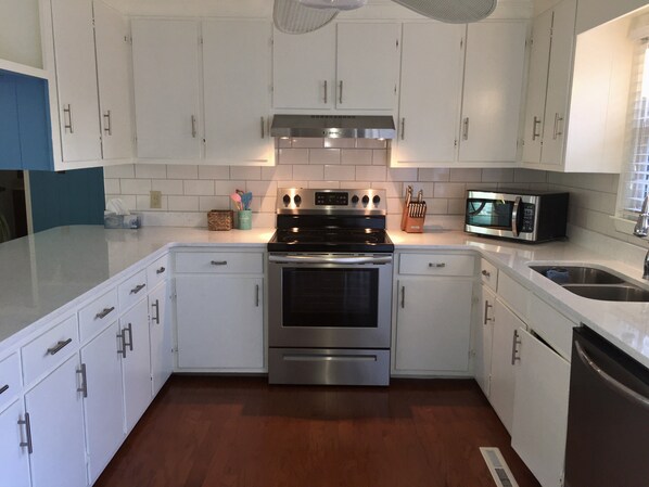 A modern kitchen with white cabinets, stainless steel appliances, and a wooden floor. - Four bedroom home and short walk to the beach! (Pine Knoll Shores)