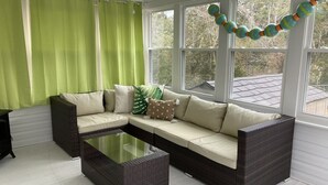 A room with a sectional sofa, a glass coffee table, and a view of trees through large windows.