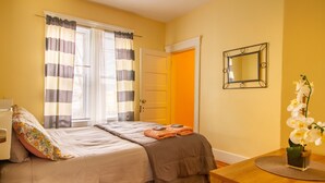 Een slaapkamer met een bed, nachtkastje, spiegel en een raam met gordijnen.