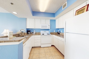 A kitchen with white cabinets, a microwave, a stove, and a refrigerator. - 17th-floor oceanfront condo with pool, hot tub, & W/D - snowbird-friendly (Myrtle Beach)