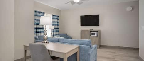 A modern living room with a sofa, a dining table, a lamp, a ceiling fan, a flat-screen TV, and a microwave.