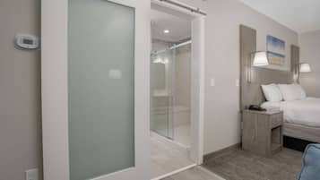 A modern hotel room with a sliding glass door leading to a shower area, a bed with a nightstand, and two wall-mounted lamps.