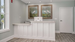 Un comptoir d’accueil avec deux tableaux encadrés représentant des oiseaux, un comptoir blanc et une porte sur la droite.