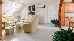 A modern living room with a sofa, armchair, and coffee table. There is a kitchen area with wooden cabinets and a brick archway.