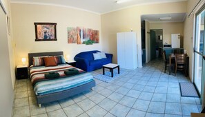 Ein kleines Hotelzimmer mit Bett, blauem Sofa, kleinem Tisch und einer Küchenzeile im Hintergrund.