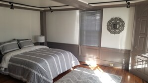 Ein Schlafzimmer mit einem Bett, einem Fenster mit Jalousien, einer Wandleuchte und einem dekorativen Spiegel.