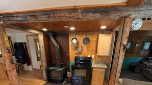 A rustic interior with a wooden floor, a fireplace, a stove, and a couch. - Escape to Priest Lake! Cabin in the woods! Air Conditioning and WiFi!! (Nordman)