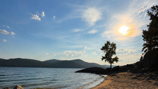 A beach with a clear sky, a sun setting or rising, and a tree on the right. - Escape to Priest Lake! Cabin in the woods! Air Conditioning and WiFi!! (Nordman)