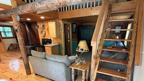 A rustic cabin interior with a wooden staircase, a sofa, a small table, and a kitchen area. - Escape to Priest Lake! Cabin in the woods! Air Conditioning and WiFi!! (Nordman)