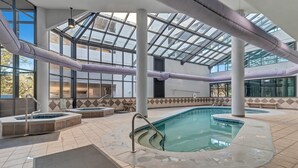 An indoor swimming pool with clear glass ceilings, multiple hot tubs, and tiled flooring.