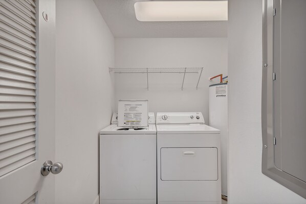 A laundry room with a front-loading washer and dryer, a metal drying rack, and a water heater.