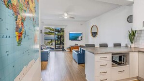A modern kitchen with a large island, a dining area with a blue sofa, and a large world map on the wall. - Beachfront self contained upstairs apartment (Semaphore)