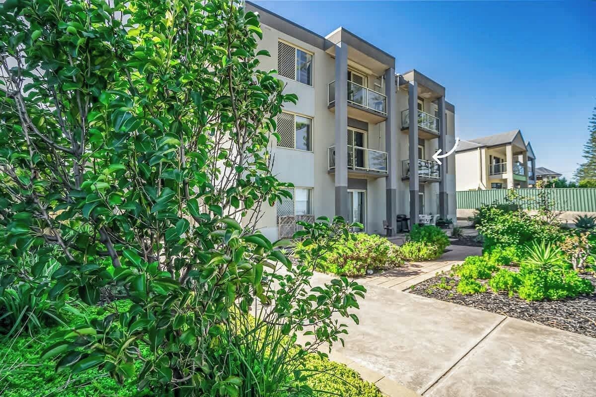 Un immeuble résidentiel à plusieurs étages, doté de balcons, d’un chemin en béton et de jardins aménagés.