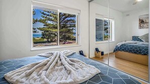 A bedroom with a large window, a bed with a geometric-patterned bedspread, and a fluffy white blanket on the floor. - Beachfront self contained upstairs apartment (Semaphore)