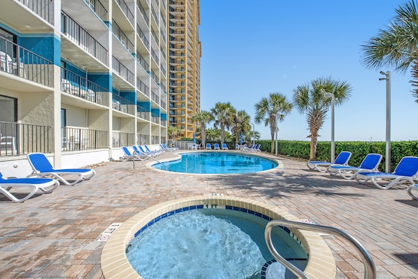 Relax by the pool surrounded by lounge chairs and a hot tub, with a view of the hotel's tall building and palm trees in the background.