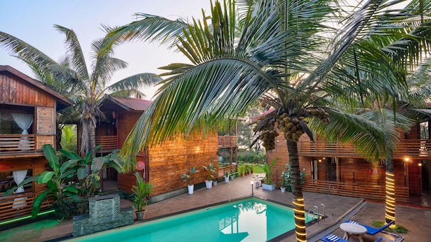 A poolside area with a wooden deck, lounge chairs, and potted plants. - Aqua Marina Beach Cottages (Candolim)