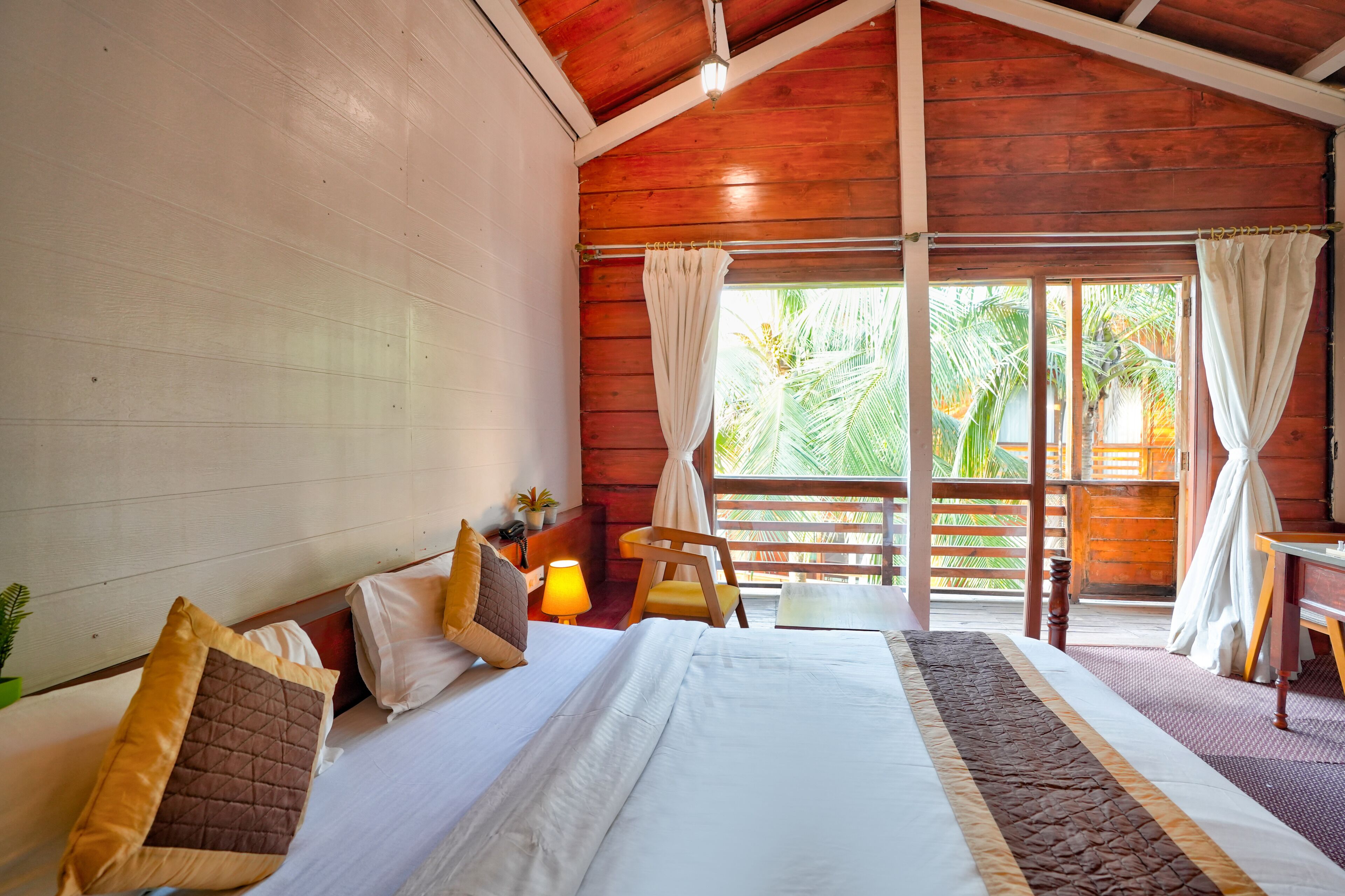 Um quarto de madeira com uma cama, uma cadeira, uma mesa e uma janela com cortinas.
