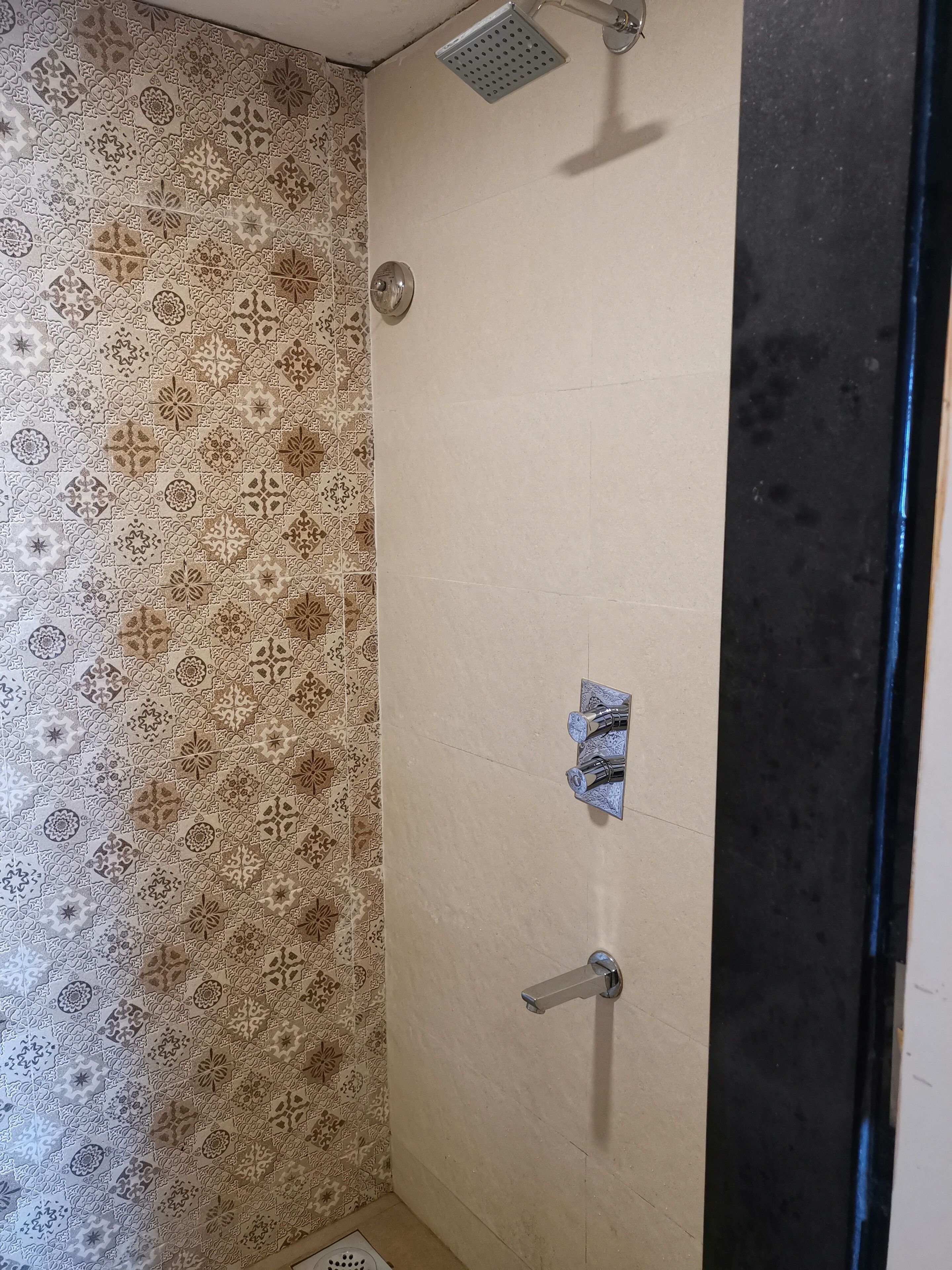 A bathroom with patterned tiles, a shower with a handheld showerhead, and a wall-mounted faucet.