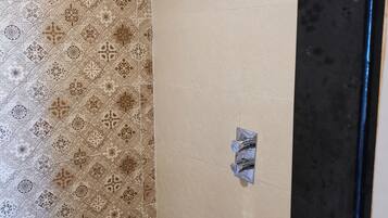 A bathroom with patterned tiles, a shower with a handheld showerhead, and a wall-mounted faucet.