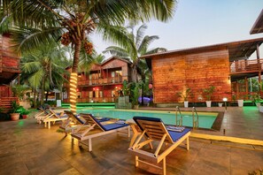 A poolside area with lounge chairs, a pool, and wooden buildings with balconies. - Aqua Marina Beach Cottages (Candolim)