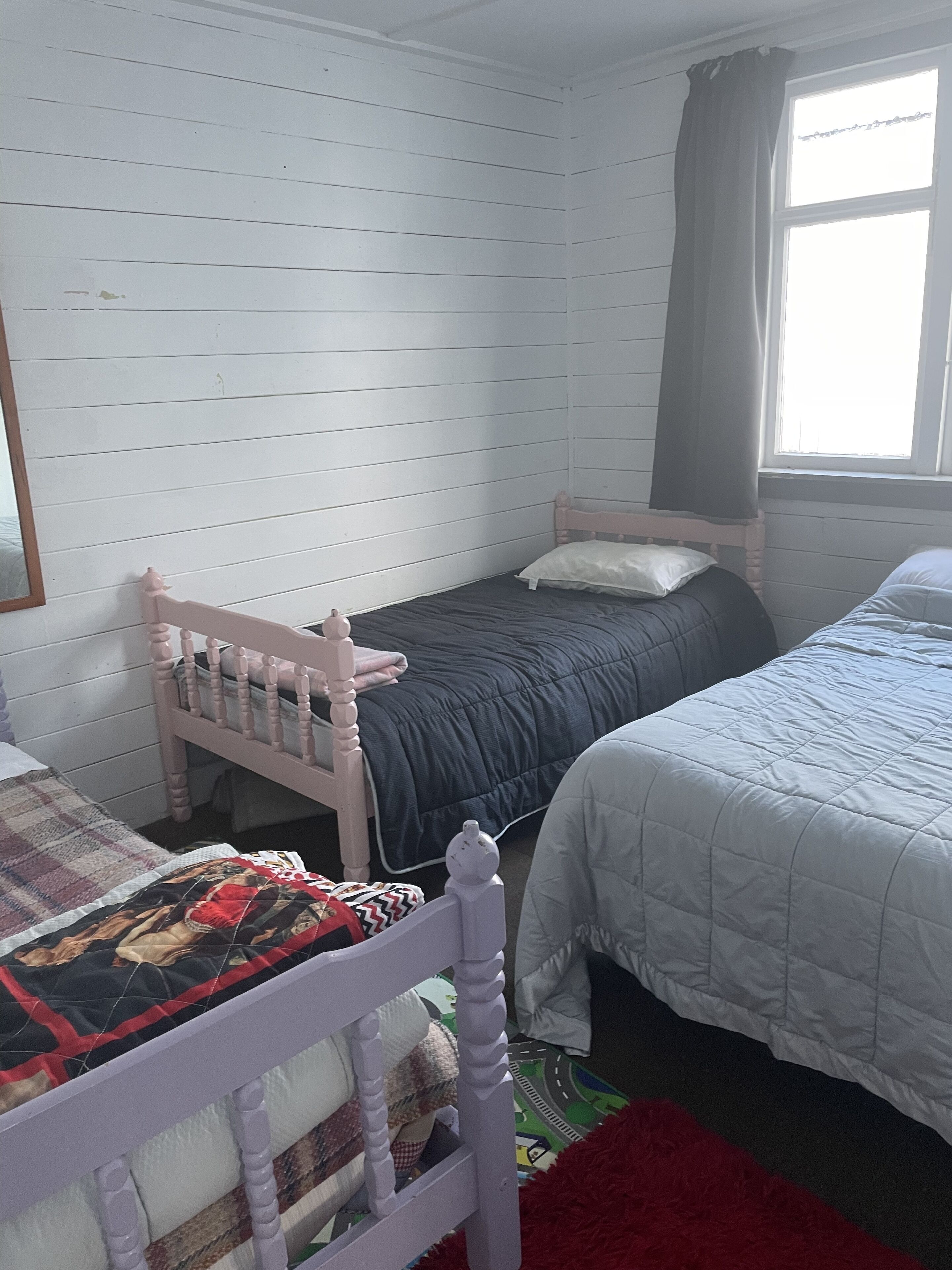 Une chambre avec deux lits, une tête de lit en bois, une fenêtre avec des rideaux et un tapis rouge.