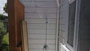 A small, enclosed outdoor shower area with a wooden door, a metal showerhead, and a window. - With the lake on your doorstep, BEACH 2 minutes away and river swimming hole . (Opunake)