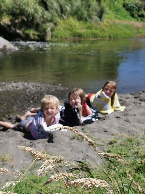Three children lying on a sandy beach near a river.