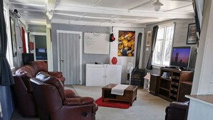 A spacious living room with a leather sofa, a wooden coffee table, and a dining area with a wooden table and chairs. - With the lake on your doorstep, BEACH 2 minutes away and river swimming hole . (Opunake)
