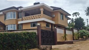 A two-story residential building with a balcony, a gated entrance, and a well-maintained hedge.