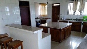 A kitchen with a central island, wooden stools, and a tiled floor.