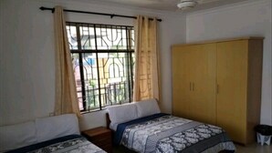 A room with two beds, a wardrobe, and a window with metal bars.