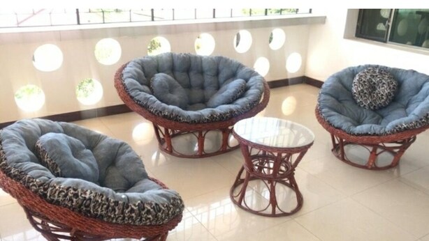 A seating area with wicker chairs and a small table, featuring a patterned cushion and a circular design on the backrest.
