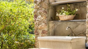 Un évier en pierre avec un robinet, un panier en osier rempli de fleurs et du feuillage verdoyant.
