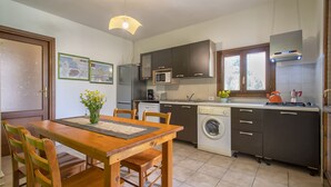 Une cuisine compacte avec des meubles de couleur sombre, un four à micro-ondes, un lave-linge et un coin repas comprenant une table et des chaises en bois.