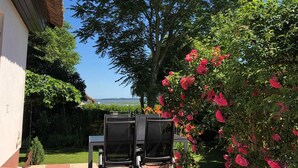An outdoor patio with a table and chairs, surrounded by lush greenery and a flowering bush. - Ferienhaus Wolff, Deutschland (Barth)