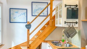 A compact kitchen with a wooden staircase, a sink, cabinets, and a trash bin. - Ferienhaus Wolff, Deutschland (Barth)