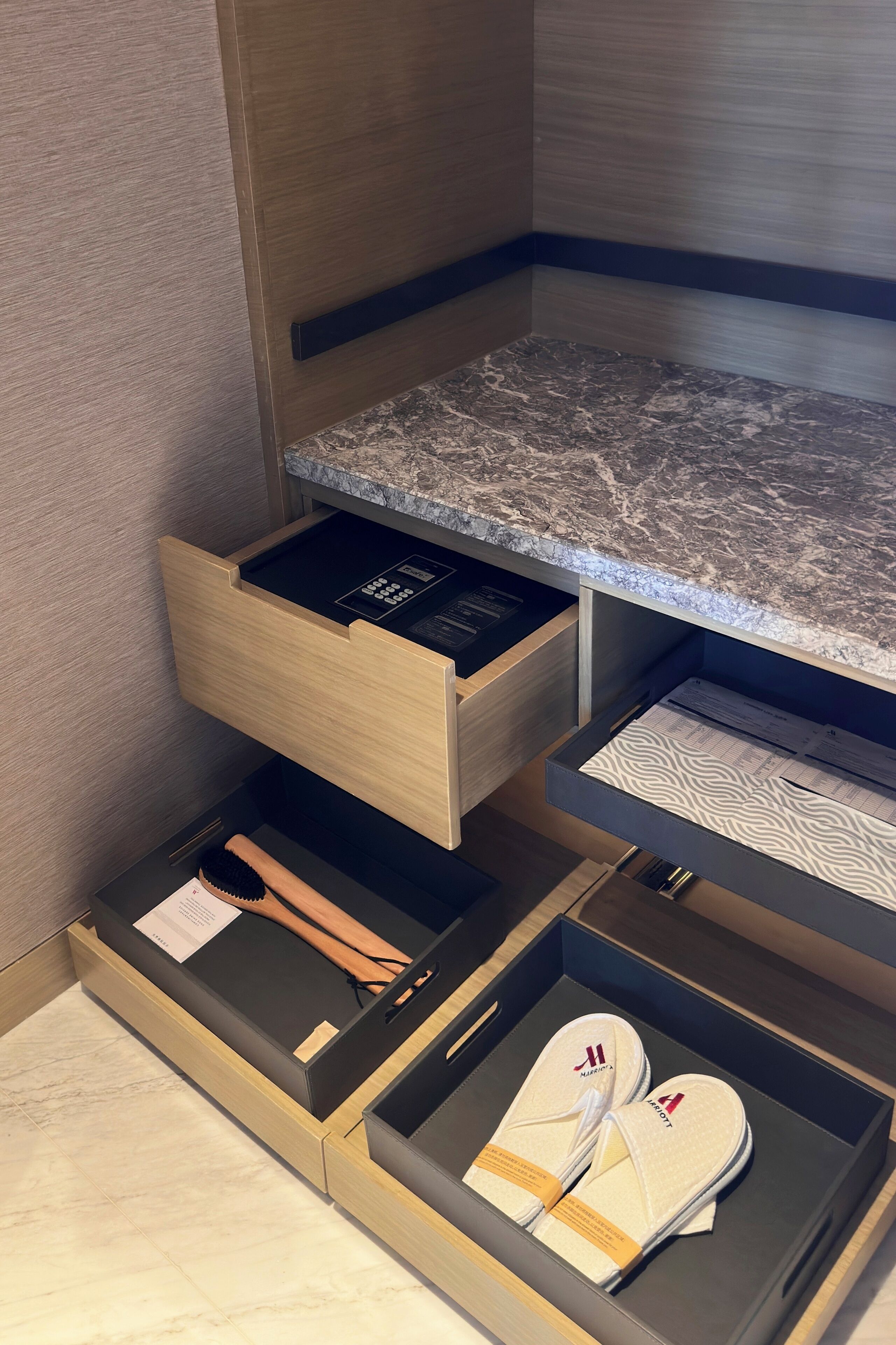 A modern bathroom with a marble countertop, wooden drawers, and a built-in shelf.
