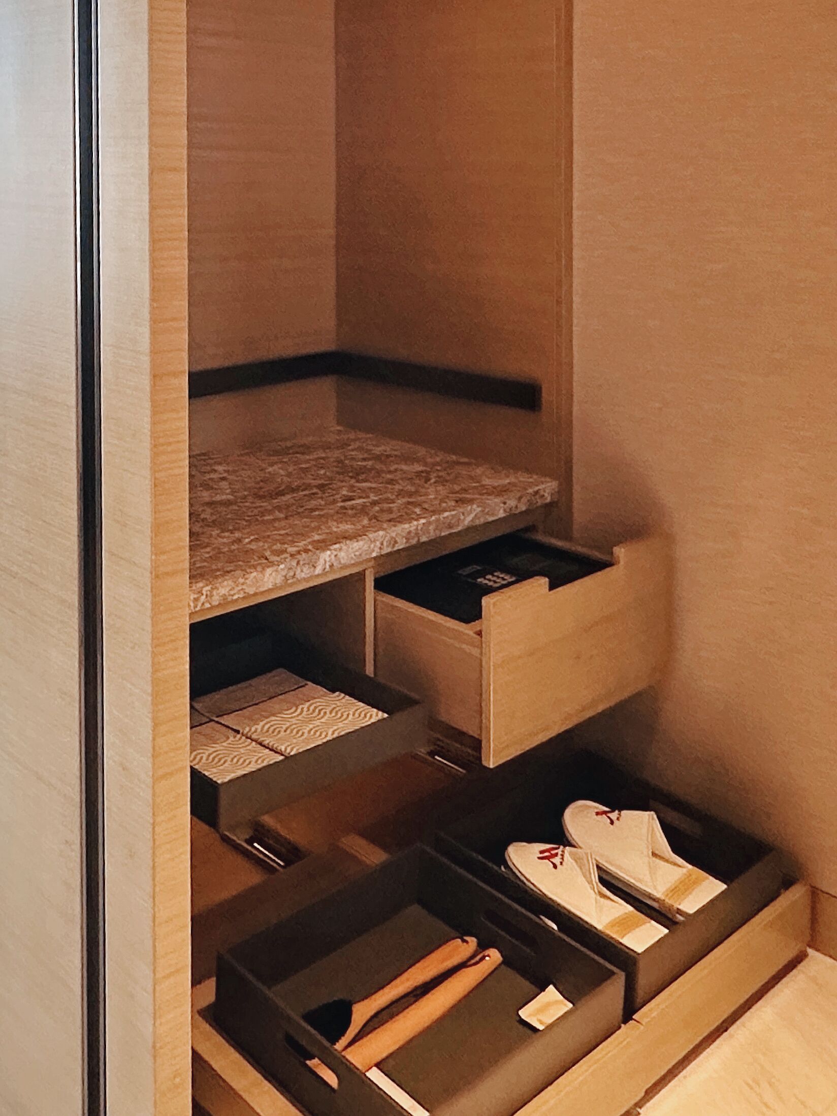 A compact storage area with multiple drawers and a shelf, containing shoes and a wooden object.