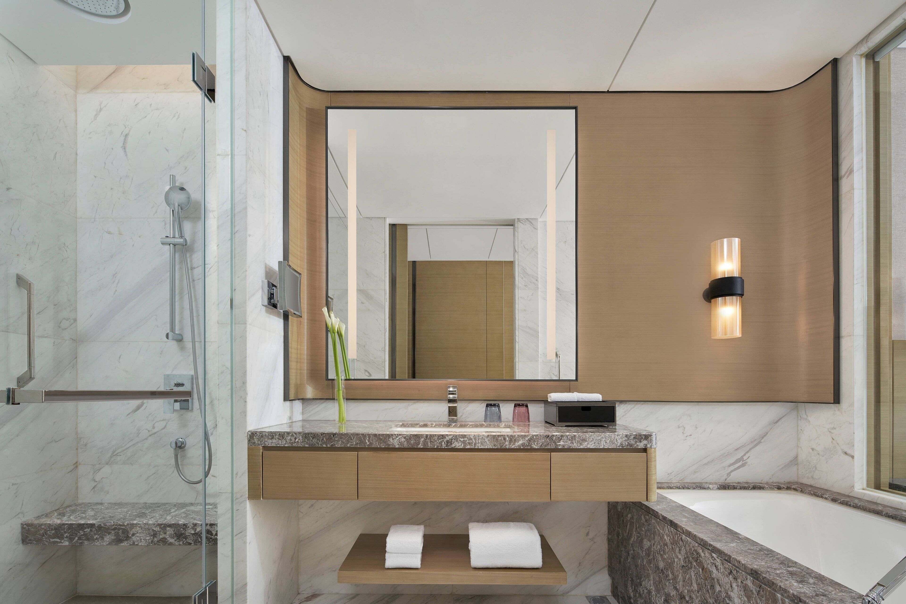 A modern bathroom with a marble vanity, a large mirror, a shower, and a bathtub.